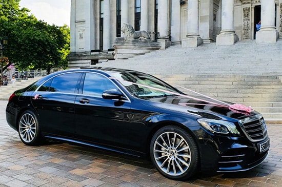A chauffeur driven Mercedes Benz salon car with wedding ribbon parked outside the wedding venue.